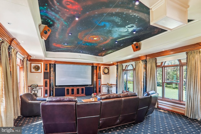 home theater room with ornamental molding, a tray ceiling, and carpet