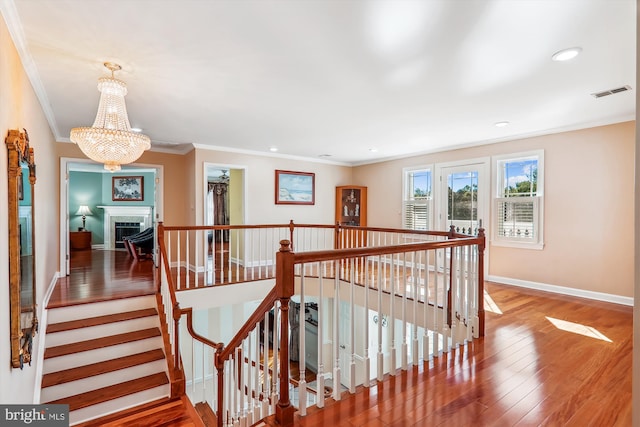 stairway featuring wood-type flooring, a chandelier, and ornamental molding