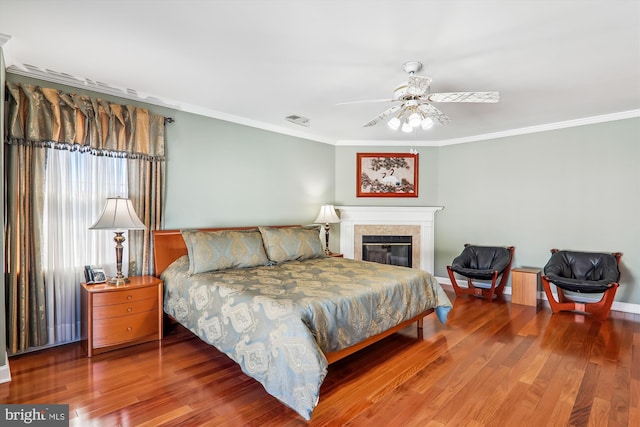 bedroom featuring hardwood / wood-style flooring, crown molding, ceiling fan, and a tile fireplace