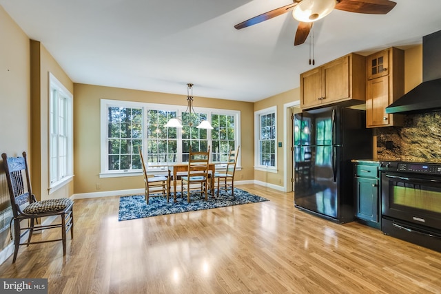 kitchen with pendant lighting, light hardwood / wood-style flooring, wall chimney range hood, and black appliances