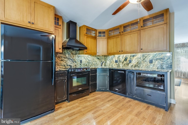 kitchen featuring light stone counters, black appliances, light hardwood / wood-style floors, wall chimney range hood, and vaulted ceiling