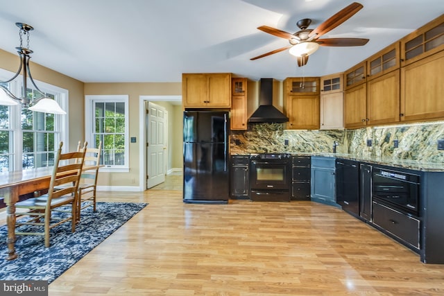 kitchen featuring hanging light fixtures, light hardwood / wood-style flooring, wall chimney exhaust hood, stone counters, and black appliances