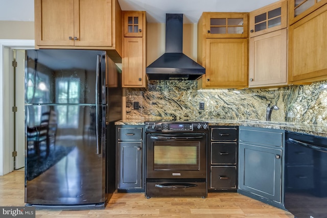 kitchen with wall chimney exhaust hood, black appliances, light stone counters, and light wood-type flooring