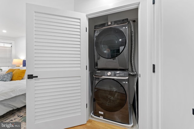 clothes washing area with wood-type flooring and stacked washer / dryer