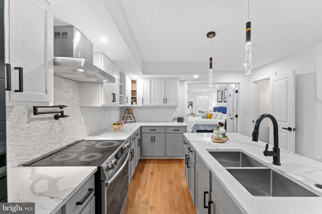 kitchen featuring tasteful backsplash, sink, wall chimney exhaust hood, light hardwood / wood-style flooring, and stainless steel electric stove