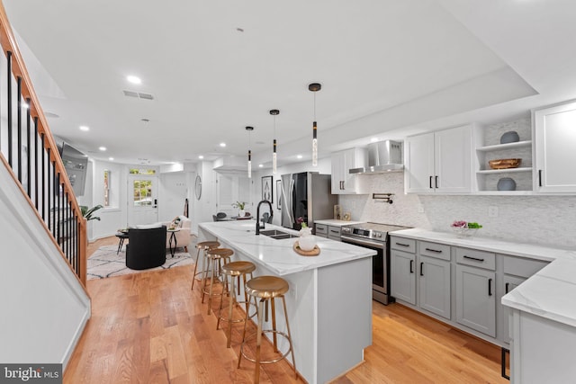 kitchen featuring light hardwood / wood-style floors, tasteful backsplash, wall chimney exhaust hood, stainless steel appliances, and a center island with sink