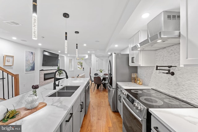 kitchen featuring light hardwood / wood-style flooring, appliances with stainless steel finishes, light stone countertops, and wall chimney range hood