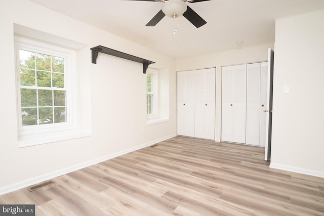 unfurnished bedroom with light wood-type flooring, multiple closets, and ceiling fan