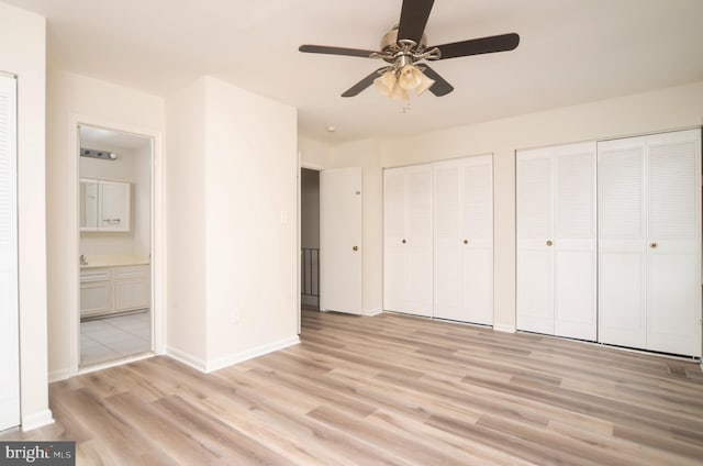 unfurnished bedroom featuring light hardwood / wood-style flooring, ensuite bathroom, ceiling fan, and two closets