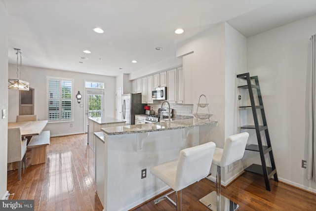 kitchen with appliances with stainless steel finishes, white cabinets, backsplash, kitchen peninsula, and pendant lighting