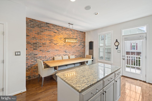 kitchen featuring light wood-type flooring, light stone counters, a center island, decorative light fixtures, and brick wall