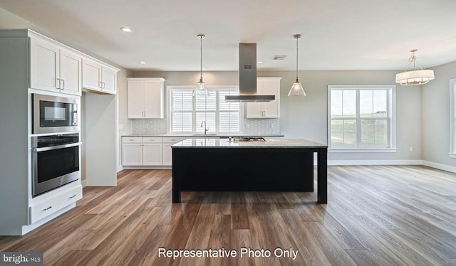 kitchen with tasteful backsplash, white cabinets, island range hood, a kitchen island, and appliances with stainless steel finishes