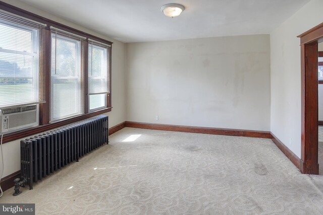 spare room with radiator heating unit, light carpet, and cooling unit