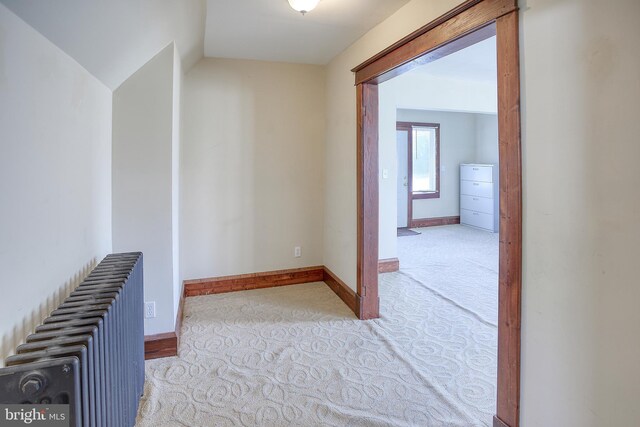 hallway with light carpet, lofted ceiling, and radiator heating unit