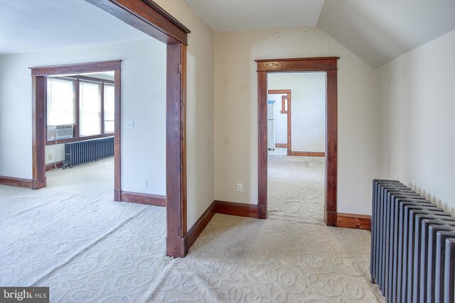 corridor with radiator heating unit, lofted ceiling, and light colored carpet