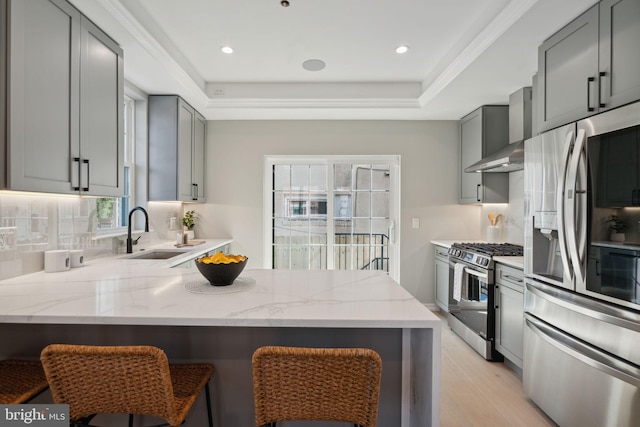 kitchen with light wood-type flooring, sink, wall chimney range hood, gray cabinetry, and appliances with stainless steel finishes