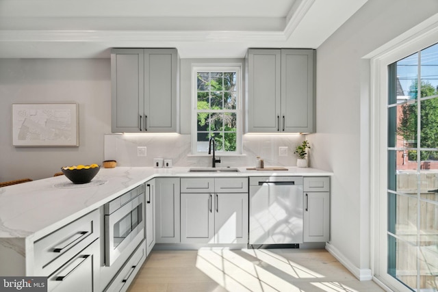 kitchen featuring appliances with stainless steel finishes, decorative backsplash, gray cabinetry, light stone counters, and sink