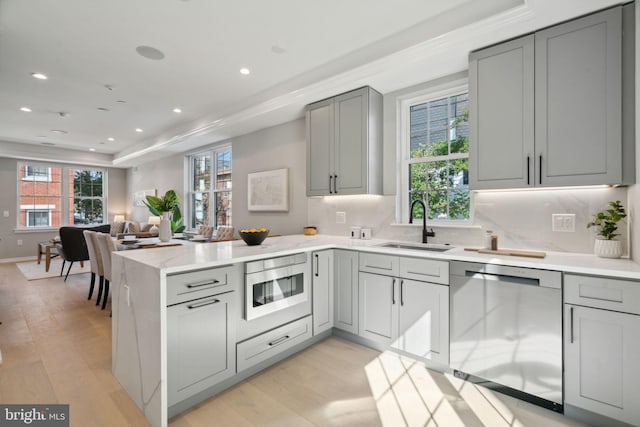 kitchen with sink, appliances with stainless steel finishes, kitchen peninsula, and light hardwood / wood-style flooring