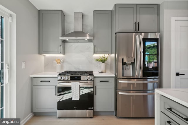 kitchen featuring stainless steel appliances, wall chimney exhaust hood, light hardwood / wood-style floors, and gray cabinetry