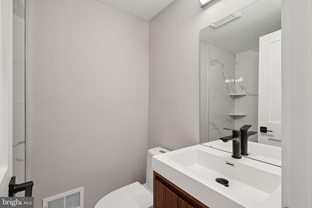 bathroom with tiled shower, vanity, and toilet