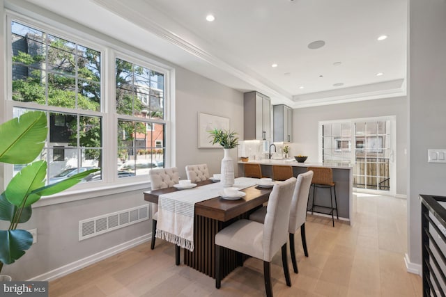 dining area featuring light wood-type flooring, a raised ceiling, and sink