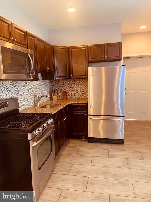 kitchen with appliances with stainless steel finishes, light stone counters, decorative backsplash, and sink