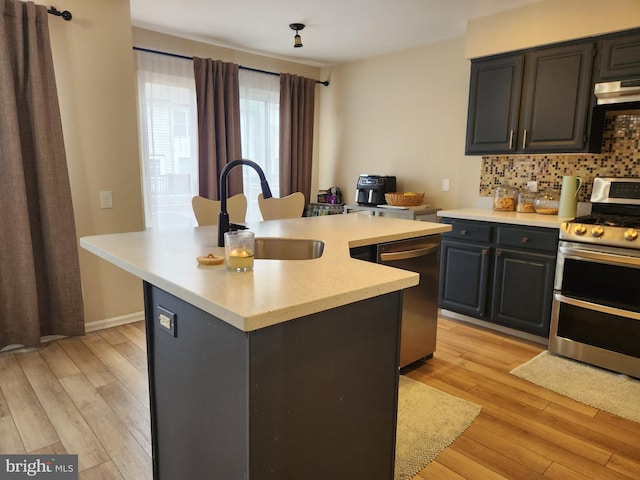 kitchen with sink, stainless steel appliances, tasteful backsplash, light hardwood / wood-style flooring, and a kitchen island with sink