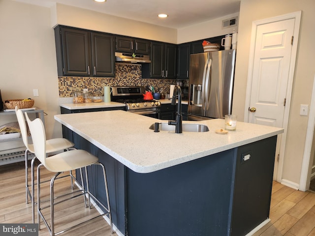 kitchen featuring light stone countertops, sink, an island with sink, light hardwood / wood-style floors, and appliances with stainless steel finishes