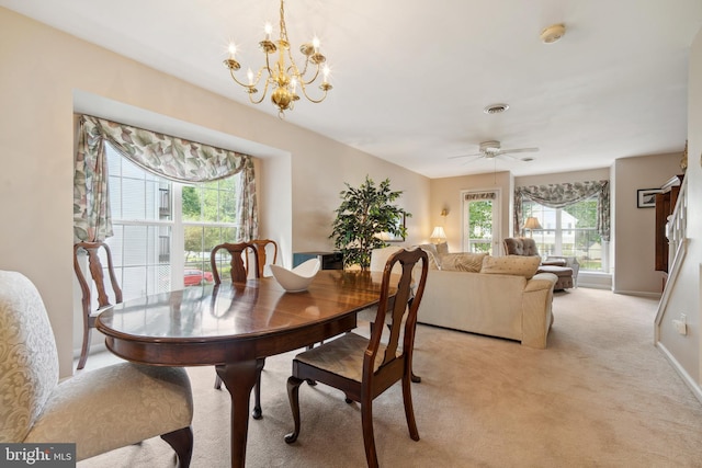 carpeted dining area with a wealth of natural light and ceiling fan with notable chandelier