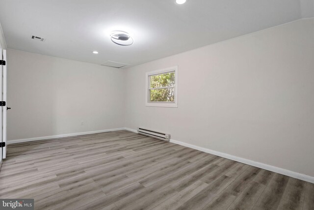 unfurnished room featuring a baseboard heating unit and light wood-type flooring