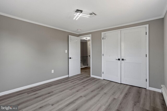 unfurnished bedroom featuring ornamental molding, a closet, a baseboard heating unit, and light hardwood / wood-style floors