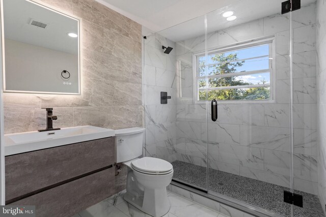 bathroom featuring vanity, toilet, tile walls, and a shower with door