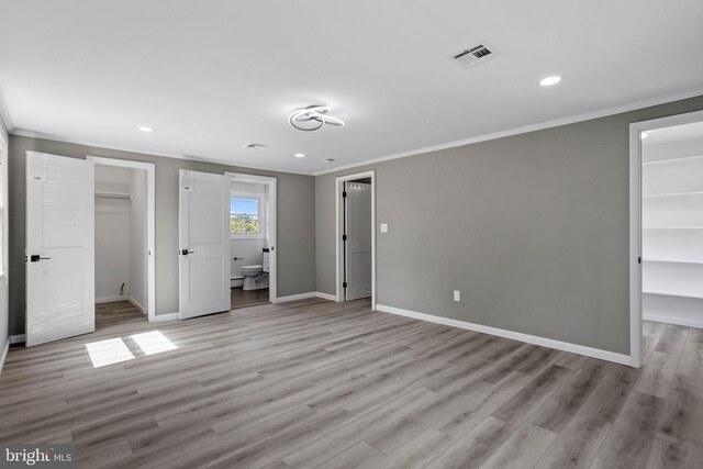 unfurnished bedroom with ornamental molding, connected bathroom, a closet, a spacious closet, and light hardwood / wood-style floors