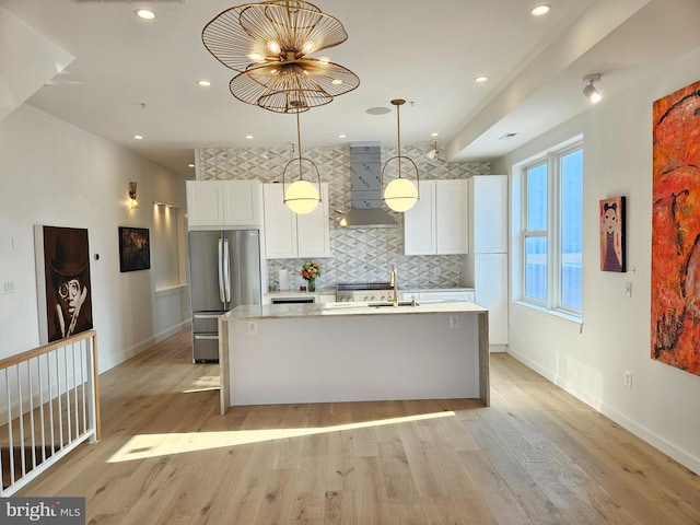 kitchen featuring white cabinets, light hardwood / wood-style flooring, an island with sink, stainless steel refrigerator, and extractor fan