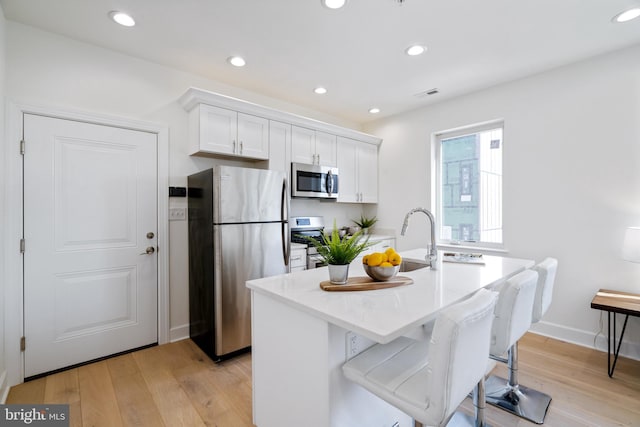 kitchen with light hardwood / wood-style flooring, stainless steel appliances, white cabinetry, an island with sink, and a kitchen breakfast bar