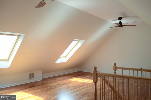 additional living space featuring a ceiling fan, visible vents, vaulted ceiling with skylight, and wood finished floors