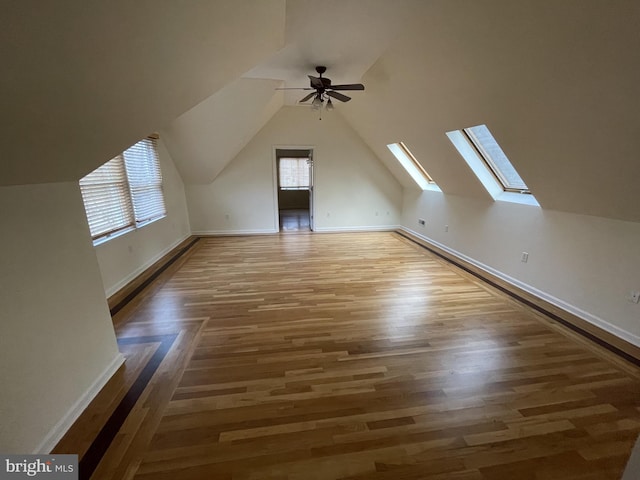 additional living space with baseboards, ceiling fan, vaulted ceiling with skylight, and wood finished floors