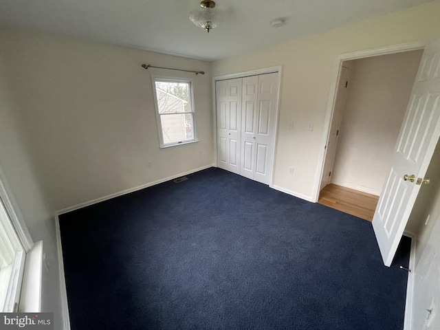 unfurnished bedroom featuring dark colored carpet, baseboards, a closet, and visible vents