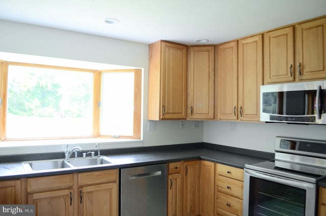 kitchen with a sink, stainless steel appliances, light brown cabinetry, and dark countertops