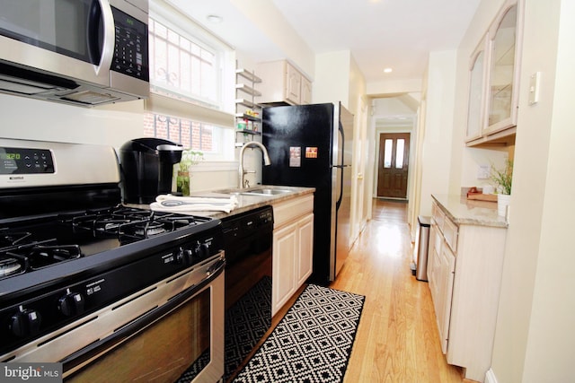 kitchen with black appliances, light hardwood / wood-style floors, light stone counters, and sink