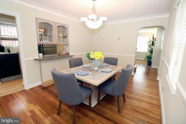 dining space with wood-type flooring, an inviting chandelier, and ornamental molding