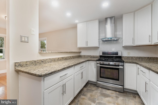 kitchen featuring white cabinets, wall chimney exhaust hood, light stone countertops, stainless steel range with gas cooktop, and decorative backsplash