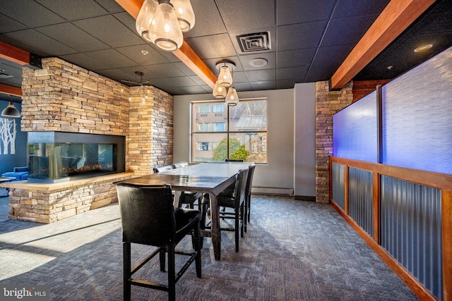 carpeted dining room with a baseboard heating unit, a drop ceiling, and a stone fireplace