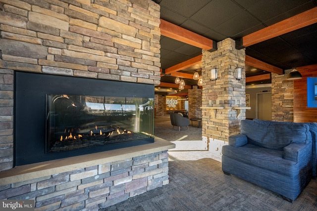 unfurnished living room with a paneled ceiling, carpet flooring, beam ceiling, and a stone fireplace