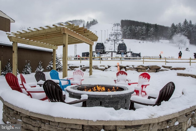 snow covered patio with a fire pit and a pergola