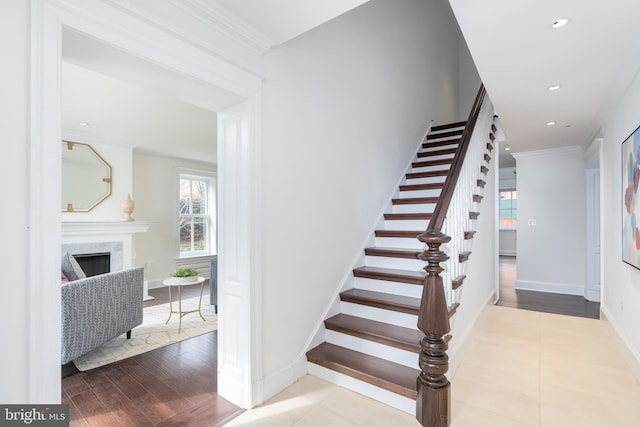 staircase featuring wood-type flooring, a premium fireplace, and crown molding