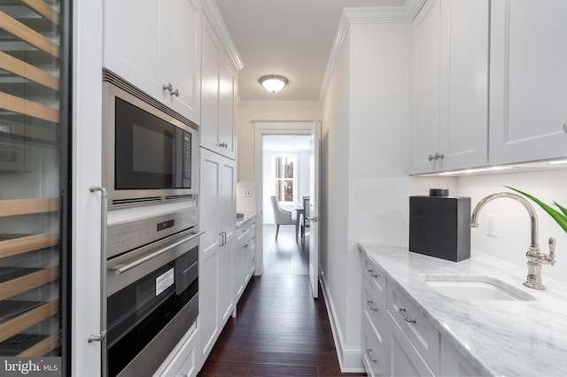 kitchen with appliances with stainless steel finishes, white cabinetry, dark wood-type flooring, light stone counters, and sink