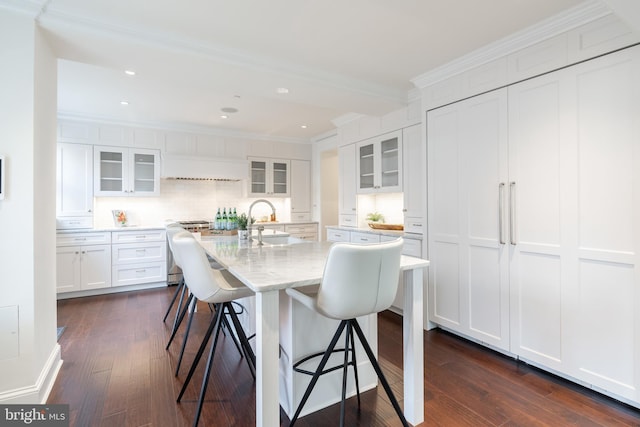 kitchen with light stone counters, dark hardwood / wood-style floors, an island with sink, white cabinetry, and crown molding