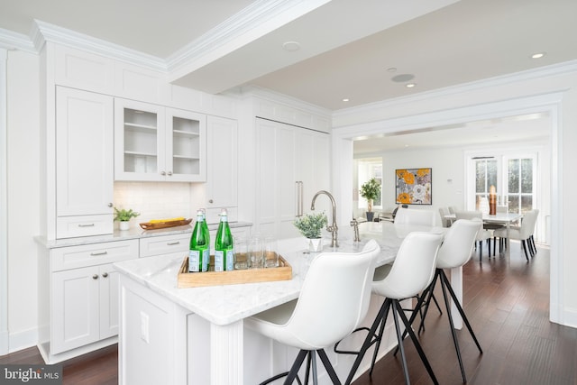 kitchen featuring an island with sink, white cabinetry, dark wood-type flooring, and crown molding