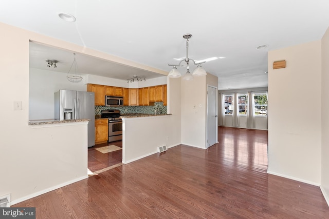 kitchen with kitchen peninsula, appliances with stainless steel finishes, decorative light fixtures, and dark hardwood / wood-style flooring